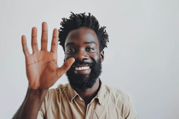 A afro American man descent warmly welcomes viewers in front of the camera, offering a friendly wave and a genuine smile against a neutral white backdrop. - obrazy, fototapety, plakaty