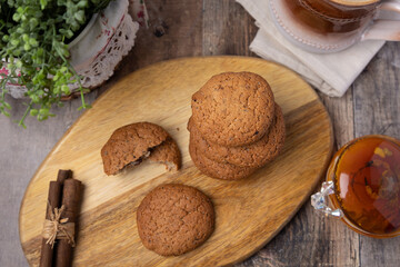 Oatmeal raisin cookies on a wooden board with cinnamon (cassia) sticks and a cup of milk. Traditional homemade pastry in rustic style. Selective focus, close-up.