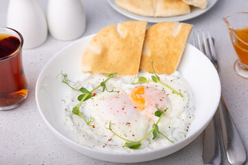 Turkish eggs (chilbir) with yogurt, fragrant butter, pea sprouts, flatbread and tea. Traditional Turkish breakfast with poached eggs (with liquid yolk). Selective focus, close-up.