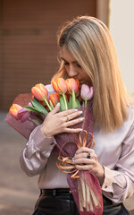 A happy woman is smelling a bouquet of spring flowers, which she holds in her hands.