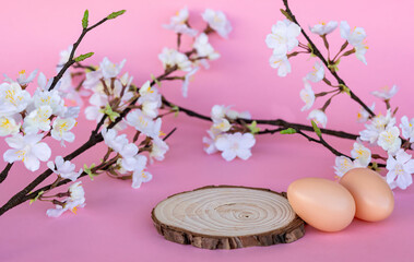 an empty wooden cutting podium for advertising your product decorated for celebration, pre-easter celebration, with easter eggs and flowered branches on pink background