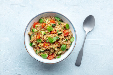 Quinoa tabbouleh salad in a bowl, a healthy dinner with tomatoes and mint, with a spoon, overhead flat lay shot