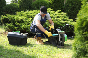 Young man cleaning lawn mower with brush in garden