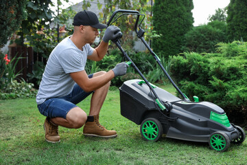 Young man fixing lawn mower in garden