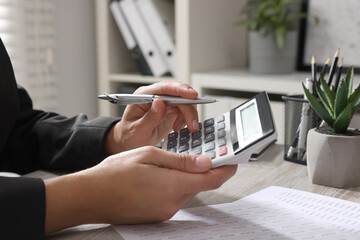 Woman using calculator at light wooden table in office, closeup