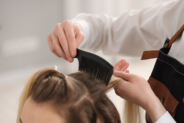 Naklejka premium Hair styling. Professional hairdresser combing woman's hair in salon, closeup