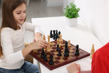Cute children playing chess at table in room