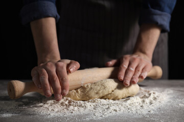Obraz na płótnie Canvas Making bread. Woman rolling dough at table on dark background, closeup