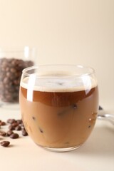 Refreshing iced coffee with milk in glass and beans on beige background, space for text