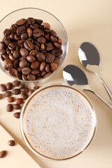 Refreshing iced coffee with milk in glass, beans and spoons on beige table, flat lay