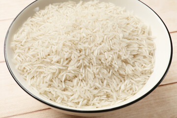 Raw basmati rice in bowl on white wooden table, closeup