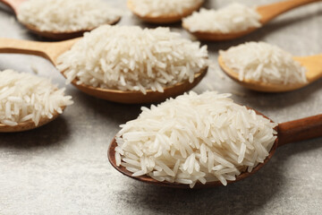 Raw basmati rice in spoons on grey table, closeup
