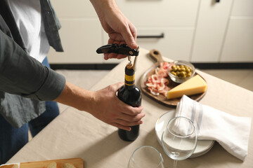 Man opening wine bottle with corkscrew at table indoors, closeup