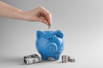 Financial savings. Woman putting coin into piggy bank on grey background, closeup