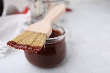 Marinade in jar and basting brush on white table, closeup. Space for text