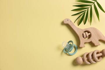 Baby accessory. Wooden rattles, pacifier and palm leaf on yellow background, flat lay. Space for...