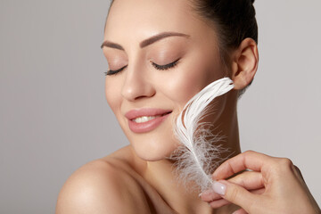 Portrait of woman with large white feather near beauty face and perfect skin on gray background. Skin care. Cosmetology, beauty and spa.