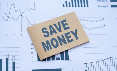 Close-up of SAVE MONEY text on brown paper over business graph paper background