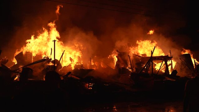 Firefighters bravely spray water on a massive fire in a rural market, using high-pressure hoses to extinguish the intense flames. Safety and disaster response are critical as they battle the blaze