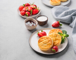Cottage cheese, cheesecakes or syrniki with strawberries, sour cream, jam and mint leaves on a white plate on a light background with napkin