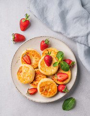Cottage cheese, cheesecakes or syrniki with strawberries and mint leaves on a white plate on a light background with napkin