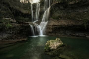 Detail of the Peñaladros waterfall, in Cozuelos, Valle de Angulo, Burgos, with a semi-submerged rock in the foreground