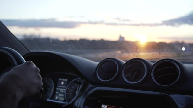 hands on steering wheel,  video of driving at the exact moment when the sun sets over the horizon line where we see the road running from inside the car.