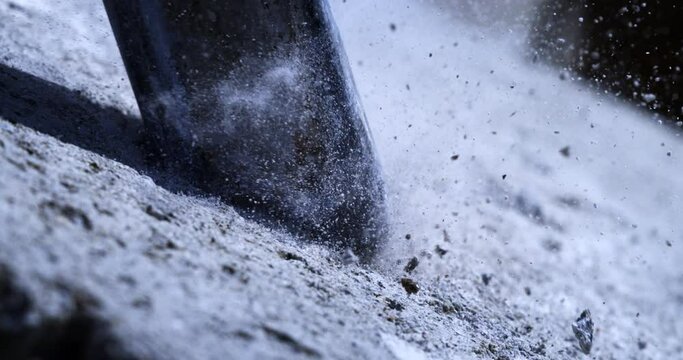 Super slow motion macro of laborer worker drilling concrete asphalt with jackhammer bit while working on road maintenance repair with flying concrete stones pieces and sand dust at 1000 fps.