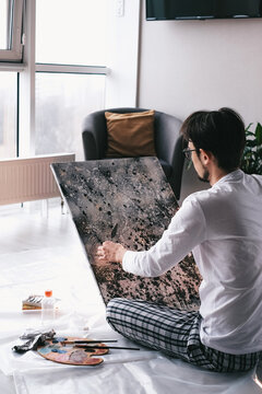 Young handsome man paints an abstract picture with oil paints