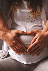 Close up photo of pregnant woman in white t-shirt and her husband make heart shape with hands on...