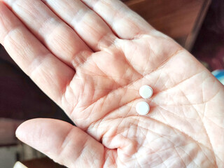 Close-up of an adult hand holding two small white pills. Close-Up of Two Pills in an Open Palm...