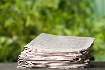 Stack of newspapers on grey table against blurred green background. Journalist's work