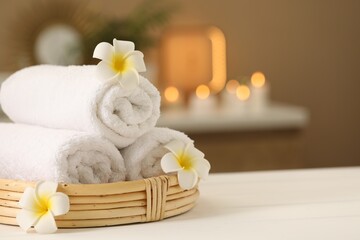 Spa composition. Rolled towels and plumeria flowers on white table indoors. Space for text