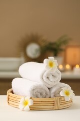 Fototapeta na wymiar Spa composition. Rolled towels and plumeria flowers on white table indoors. Space for text