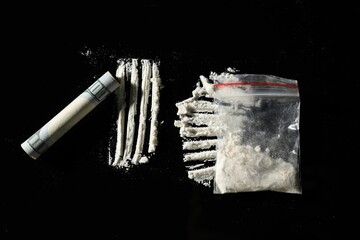 Drug addiction. Plastic bag with cocaine and rolled dollar banknote on black background, flat lay