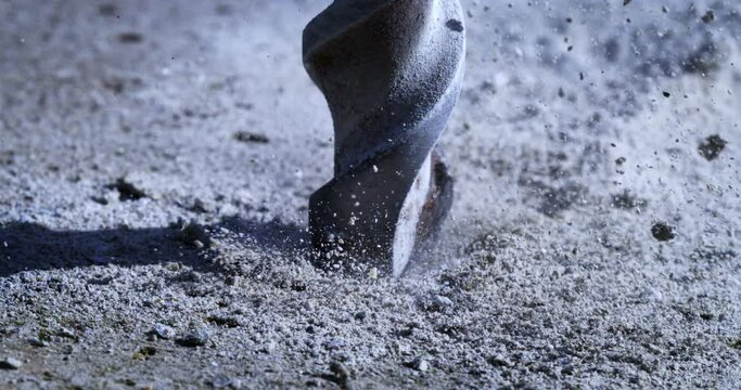 Super slow motion close up of laborer worker drilling concrete asphalt with jackhammer bit while working on road maintenance repair with flying concrete stones pieces and sand dust at 1000 fps.