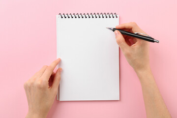 Woman writing in notebook on pink background, top view