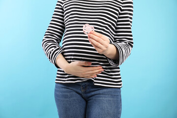Pregnant woman with pacifier on light blue background, closeup