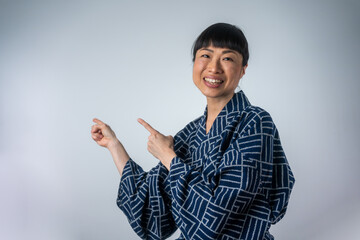 Photo of happy asian woman standing isolated over white wall background. Looking camera showing copyspace pointing. 