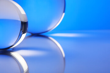 Transparent glass balls on mirror surface against blue background, closeup