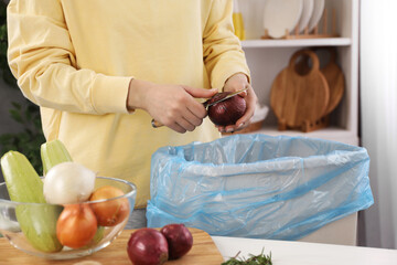 Woman peeling fresh onion above garbage bin indoors, closeup