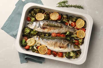 Delicious fish with vegetables and lemon in baking dish on light marble table, top view