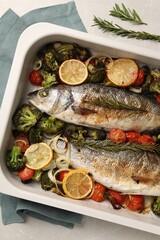 Delicious fish with vegetables and lemon in baking dish on light marble table, top view