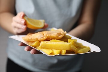 Woman adding lemon to delicious fish and chips on gray background, closeup