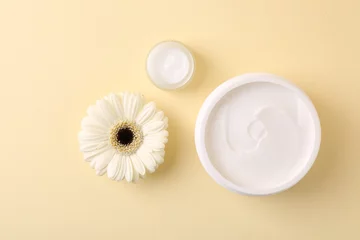Foto op Plexiglas Moisturizing cream in open jars and gerbera flower on beige background, flat lay. Body care product © New Africa