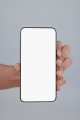 Man holding smartphone with blank screen on grey background, closeup