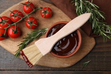 Marinade in bowl, basting brush, tomatoes and rosemary on wooden table, flat lay