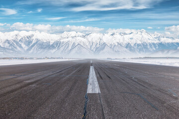 Empty airport runway at winter day on the background of high scenic snow capped mountains