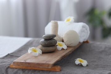 Stacked spa stones, flowers, herbal bags and towel on massage table indoors