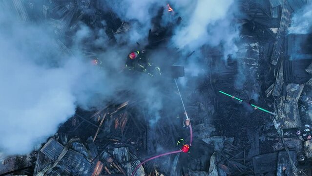 Firefighters bravely spray water on a massive fire in a rural market, using high-pressure hoses to extinguish the intense flames. Safety and disaster response are critical as they battle the blaze